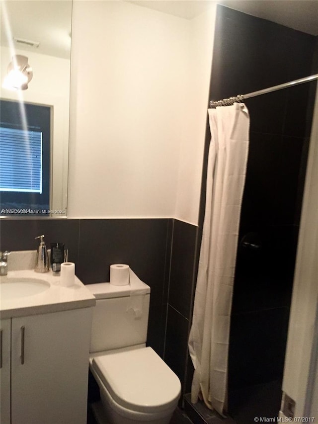 full bath featuring toilet, a wainscoted wall, a tile shower, and vanity