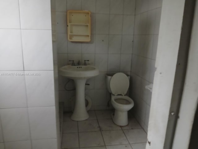 bathroom with toilet, tile patterned flooring, tile walls, and a sink