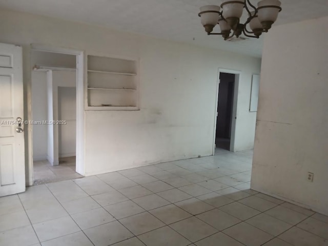 spare room with light tile patterned floors, built in features, and a chandelier