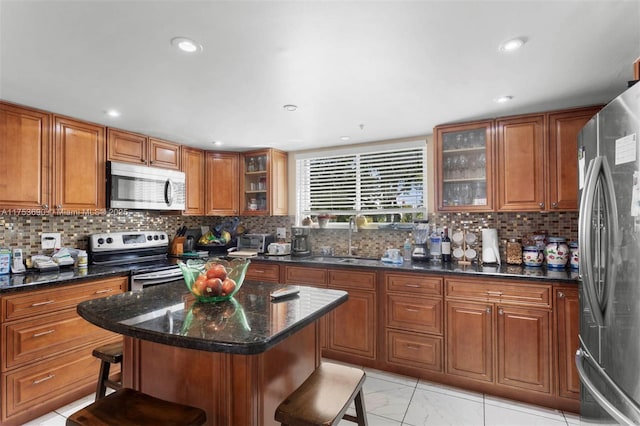 kitchen with brown cabinetry, a breakfast bar area, a sink, stainless steel appliances, and backsplash