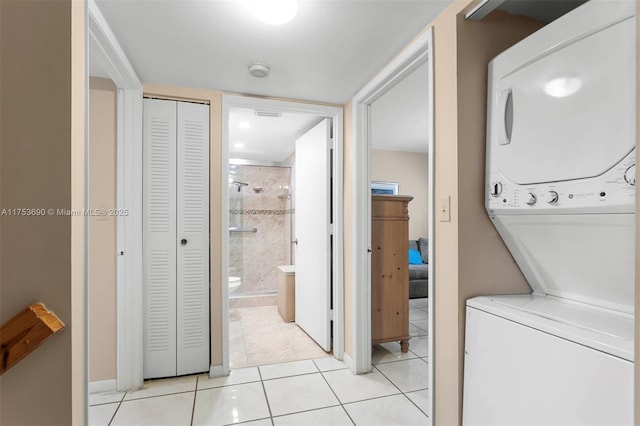 laundry room with stacked washer / drying machine, laundry area, baseboards, and light tile patterned floors