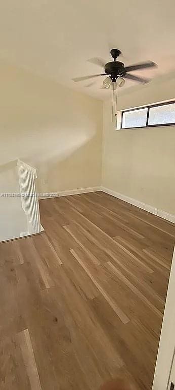 empty room featuring wood finished floors, a ceiling fan, and baseboards