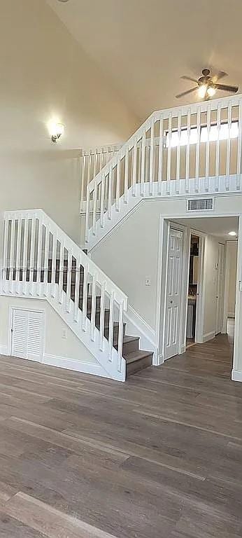 stairs with baseboards, visible vents, a towering ceiling, ceiling fan, and wood finished floors