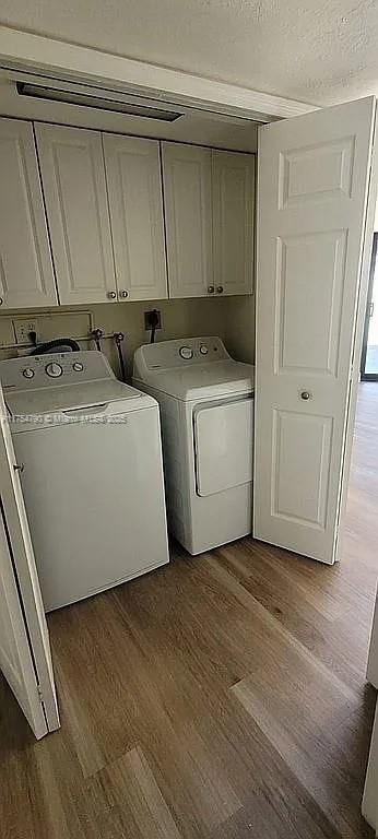 clothes washing area with a textured ceiling, dark wood finished floors, washing machine and dryer, and cabinet space