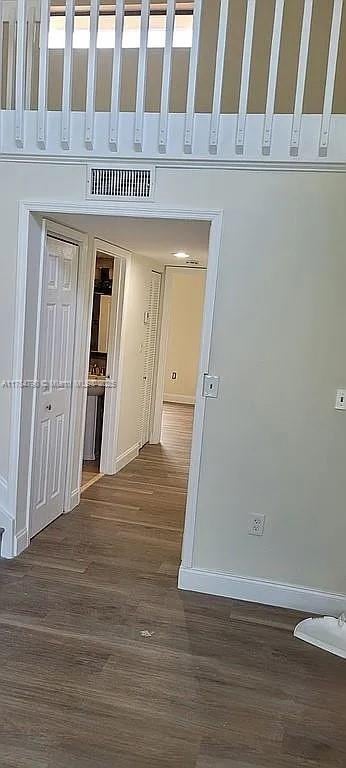 hall featuring dark wood-style flooring, visible vents, and baseboards