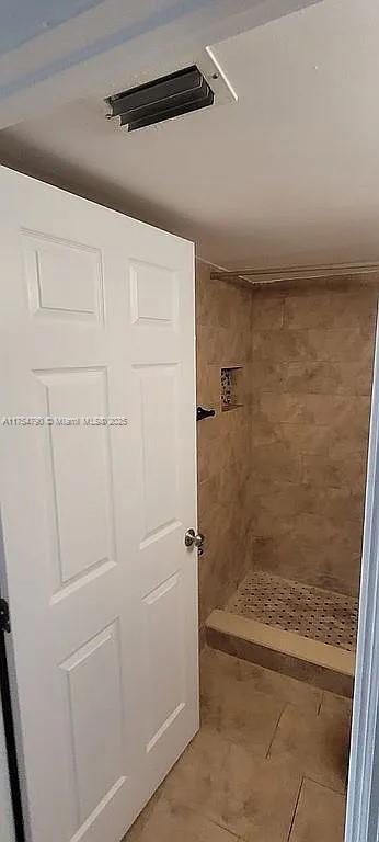 full bathroom featuring tiled shower and visible vents