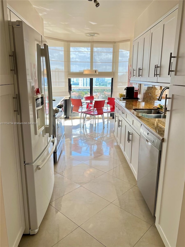 kitchen featuring stone countertops, expansive windows, a sink, white refrigerator with ice dispenser, and dishwasher