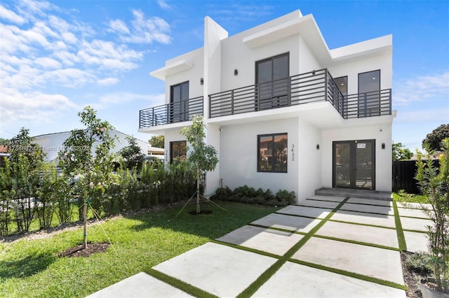 view of front facade with a balcony, stucco siding, a front lawn, and french doors