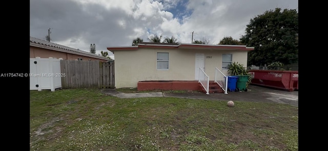 back of property with a lawn, fence, and stucco siding