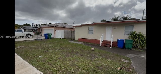 view of side of home with a garage, an outdoor structure, concrete driveway, a lawn, and stucco siding