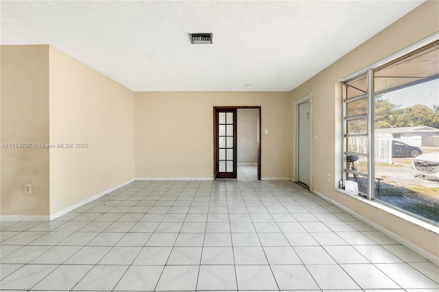 spare room featuring light tile patterned floors, baseboards, visible vents, and a textured ceiling