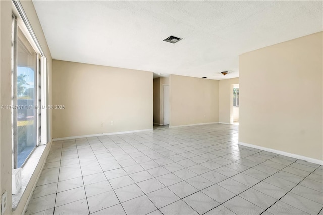 empty room with a textured ceiling, light tile patterned floors, visible vents, and baseboards