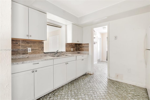 kitchen featuring a sink, white cabinetry, baseboards, light floors, and tasteful backsplash