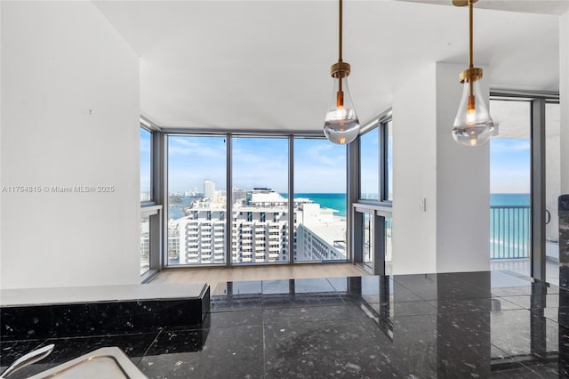 interior space with expansive windows, a water view, hanging light fixtures, and a view of city