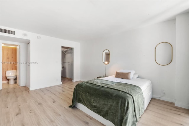 bedroom with light wood-type flooring, visible vents, a spacious closet, and baseboards