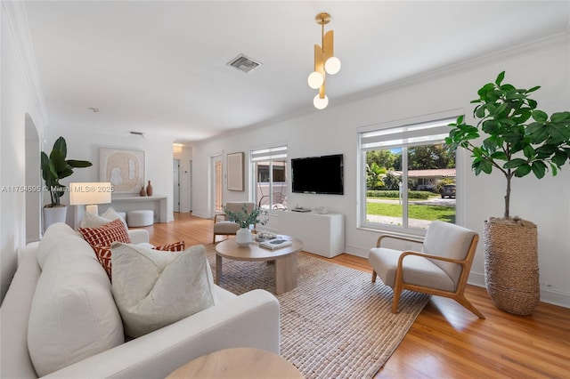 living room with ornamental molding, light wood finished floors, visible vents, and baseboards