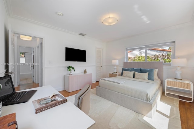 bedroom with wood finished floors, visible vents, and crown molding