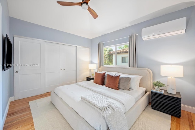 bedroom with baseboards, a ceiling fan, an AC wall unit, light wood-style floors, and a closet