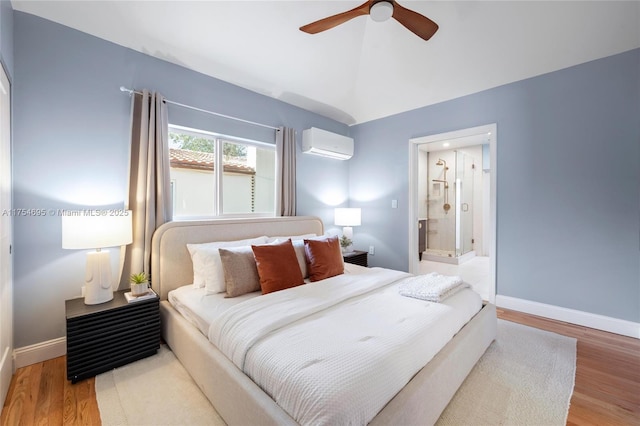 bedroom featuring a wall unit AC, vaulted ceiling, baseboards, and wood finished floors