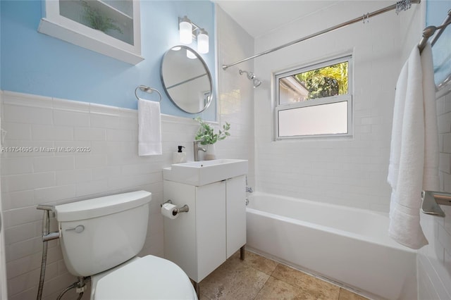 bathroom featuring bathtub / shower combination, toilet, vanity, tile walls, and wainscoting