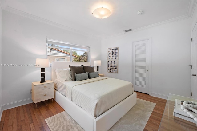 bedroom featuring ornamental molding, visible vents, baseboards, and wood finished floors