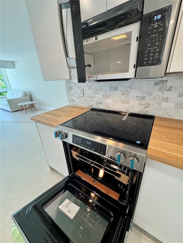 555 Crandon Blvd Unit 32, Key Biscayne, FL 33149 - kitchen view of electric stove, backsplash, stainless steel microwave, wooden counters, and white cabinets