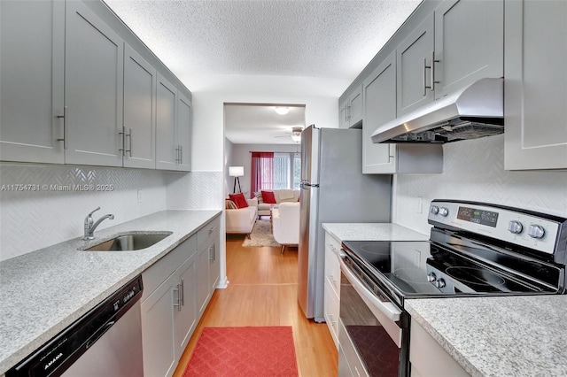 kitchen with under cabinet range hood, stainless steel appliances, a sink, light countertops, and light wood finished floors