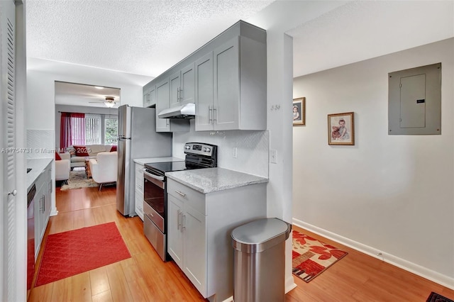 kitchen with stainless steel appliances, light wood-style floors, a textured ceiling, electric panel, and under cabinet range hood