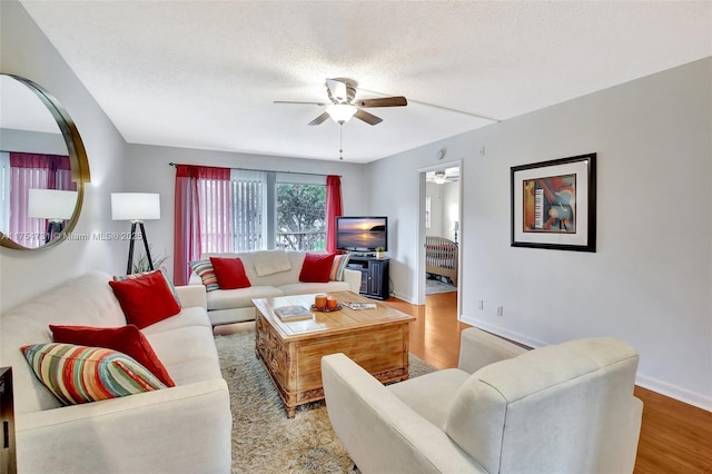 living area with ceiling fan, a textured ceiling, baseboards, and wood finished floors