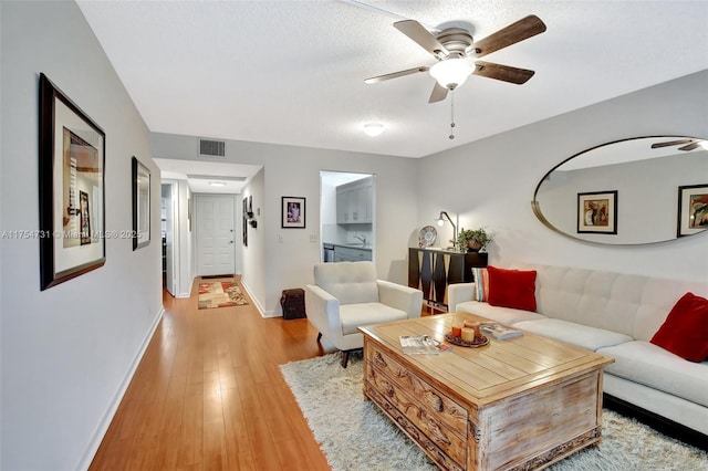 living area with ceiling fan, wood finished floors, visible vents, and baseboards