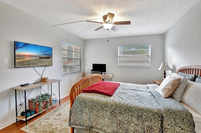 bedroom with a ceiling fan, a textured ceiling, baseboards, and wood finished floors