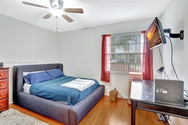 bedroom featuring light wood-style floors, a textured ceiling, baseboards, and a ceiling fan