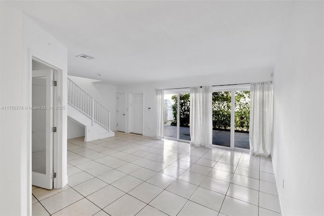 empty room featuring light tile patterned floors, visible vents, and stairs