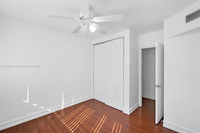 unfurnished bedroom with baseboards, visible vents, dark wood finished floors, ceiling fan, and a closet