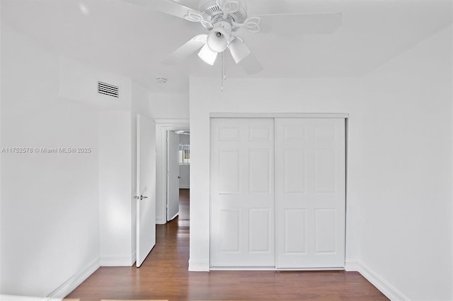 unfurnished bedroom featuring dark wood-style floors, baseboards, visible vents, and a closet