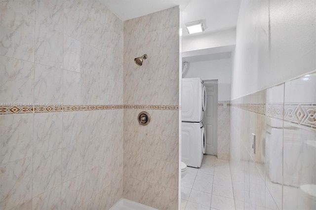 full bathroom with tiled shower, tile patterned flooring, tile walls, and stacked washer / drying machine