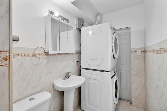 half bath featuring toilet, tile patterned floors, tile walls, and stacked washer / drying machine