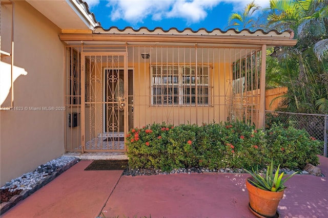 doorway to property featuring fence, a tiled roof, and stucco siding