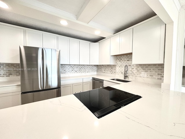 kitchen with a sink, white cabinetry, appliances with stainless steel finishes, decorative backsplash, and light stone countertops