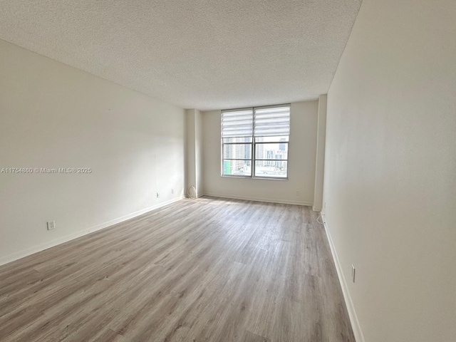 empty room with a textured ceiling, baseboards, and wood finished floors