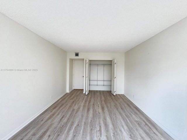 empty room featuring light wood-style floors, baseboards, visible vents, and a textured ceiling