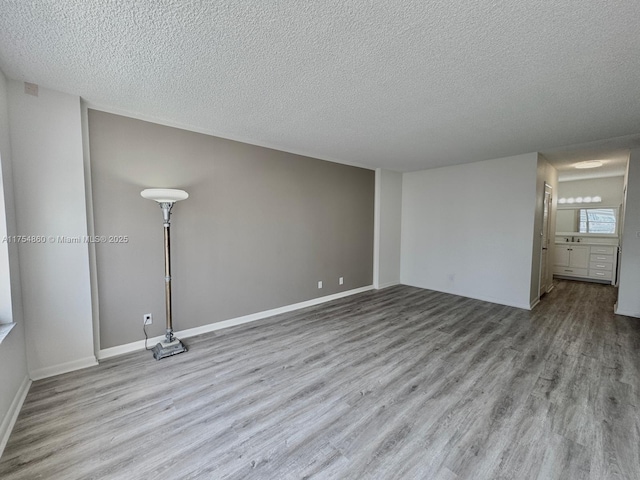 empty room with a textured ceiling, baseboards, and wood finished floors