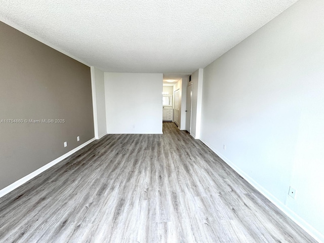 unfurnished room featuring a textured ceiling, wood finished floors, and baseboards