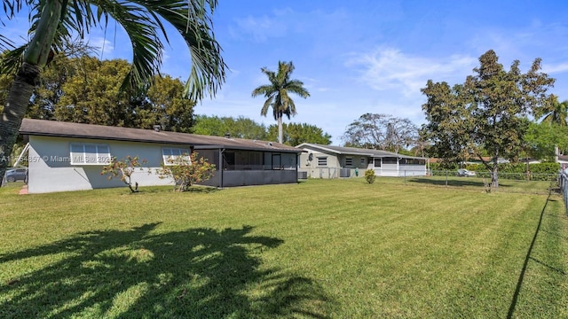 rear view of house featuring a lawn, fence, a sunroom, and stucco siding