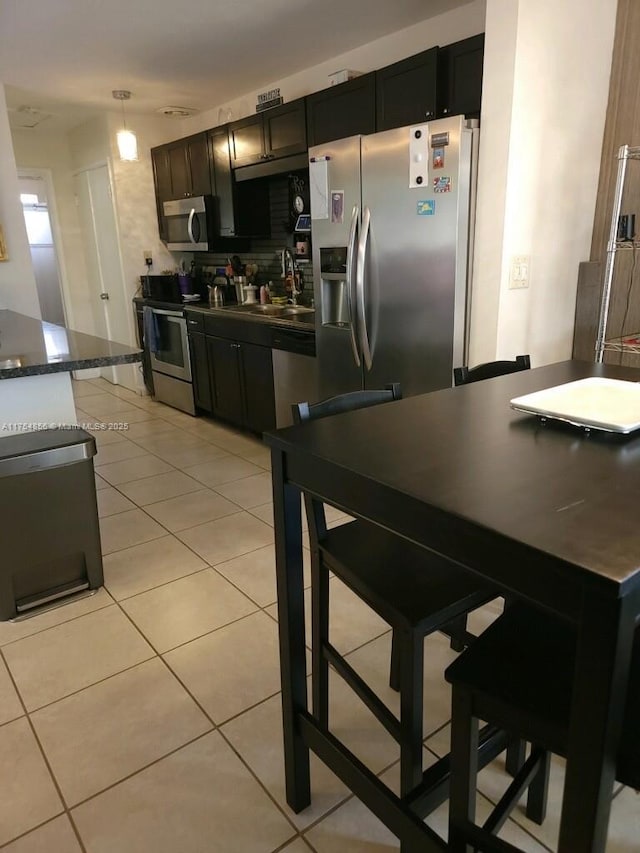 2217 NE 14th Ave, Wilton Manors, FL 33305 - kitchen featuring light tile patterned floors, stainless steel appliances, a sink, dark countertops, and pendant lighting