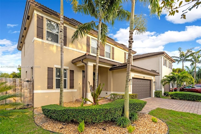 view of front facade featuring a garage, decorative driveway, fence, and stucco siding