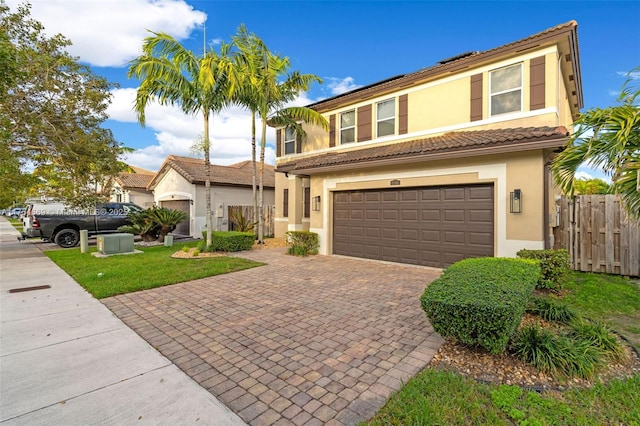 view of front of home featuring an attached garage, fence, decorative driveway, roof mounted solar panels, and stucco siding