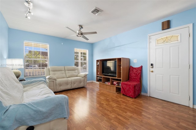 living area with a ceiling fan, wood finished floors, visible vents, and baseboards