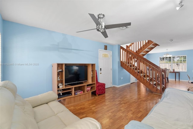 living room with stairs, visible vents, wood finished floors, baseboards, and ceiling fan with notable chandelier