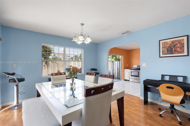 dining space with arched walkways, visible vents, light wood-style flooring, an inviting chandelier, and baseboards